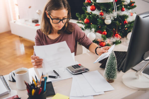 Woman paying off holiday bills in the living room with a Christmas tree