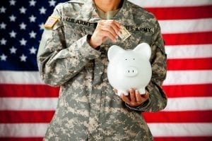 Soldier holding managing finances by putting money in a piggy bank
