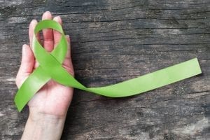 Hand holding green ribbon as symbol of mental health awareness