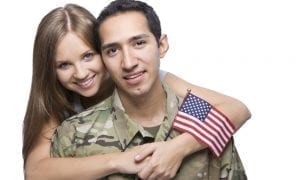 Military husband in uniform being hugged by his spouse holding a mini American flag