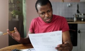 Closeup of young African American man sitting at table trying to understand such great sums in his bills