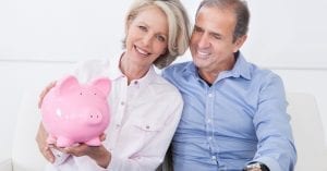 Happy smiling older couple sitting together on couch calculating coins in piggy-bank