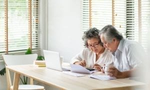 Stressed senior Asian couple looking over papers, calculator and laptop to pay bills