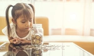 Young girl leaning on table looking over scattered coins and a jar of coins