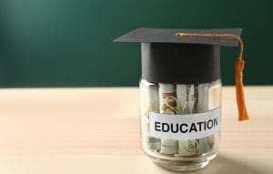 Glass jar with money for education on wooden table against green background