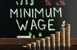 Minimum wage written on blackboard behind rising stack of coins