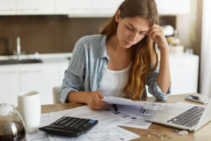 Woman with credit card bills on kitchen table wondering what would happen if she stopped paying them