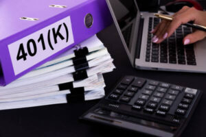 Word 401 K is written on a folder lying on documents on an office desk with a laptop and a calculator.