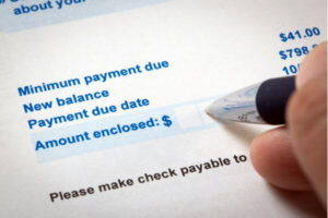 Credit card statement bill showing the minimum payment with a hand and pen.