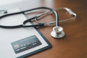 Credit card and stethoscope resting on clipboard in clinical workspace, representing medical bills affect your credit