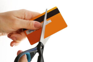 Hand cutting a credit card with a scissors representing closing a credit card.
