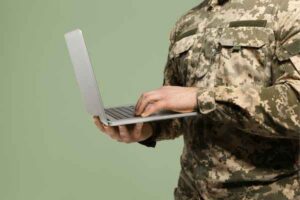 Soldier with laptop on green background, representing military loan application.