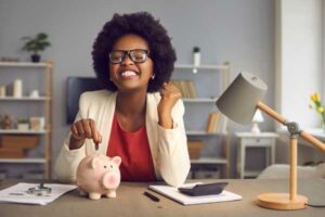 Woman smiling as she adds a coin to a piggy bank, representing the start of a savings plan.